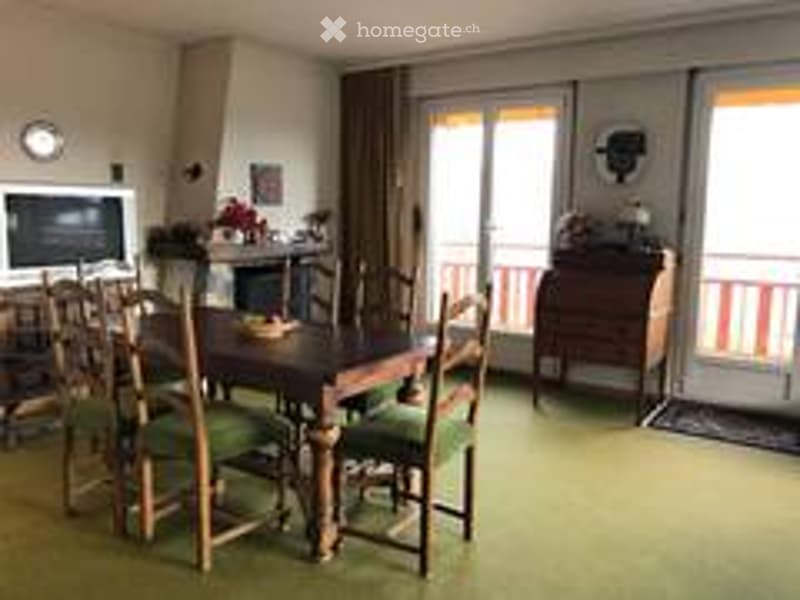 Dining room with a wooden dining table and chairs, a television, and a cabinet, with large windows and a balcony view.