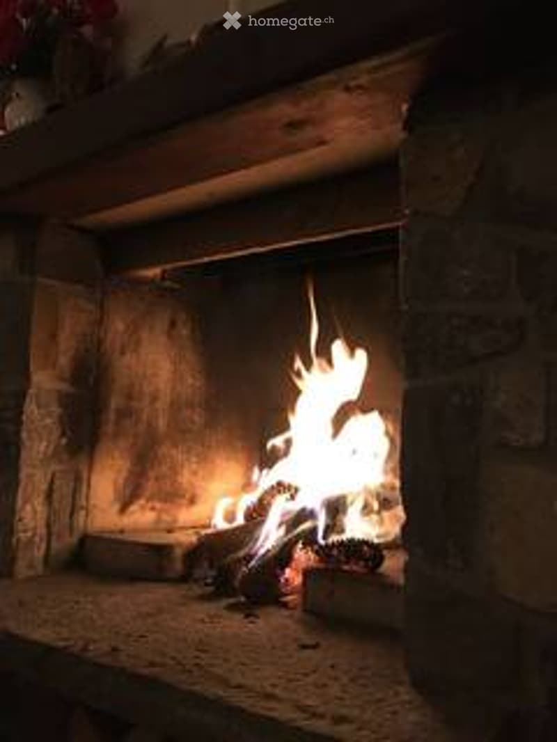 A stone fireplace with a roaring fire, surrounded by brick walls and a wooden mantel.