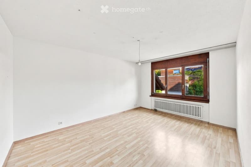 Empty room with light wooden flooring, white walls, and a large window with wooden frame and radiator below.