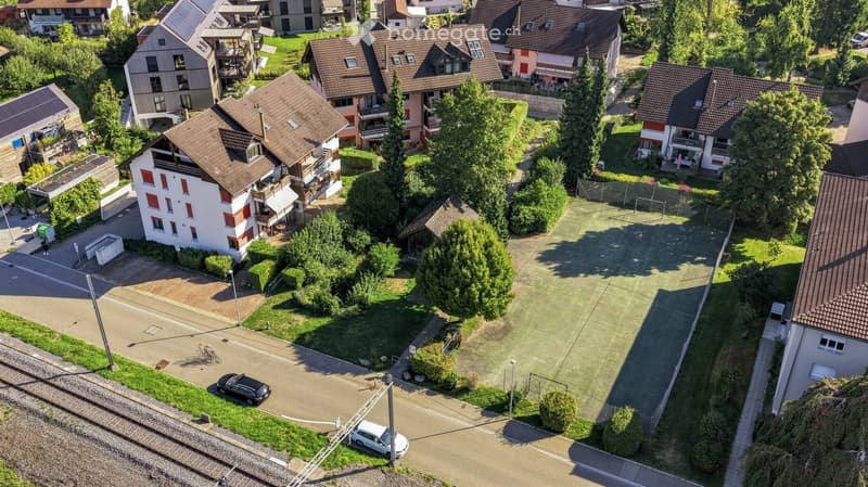 Aerial view of a residential neighborhood with multiple houses, gardens, and a central open area with a sports field.