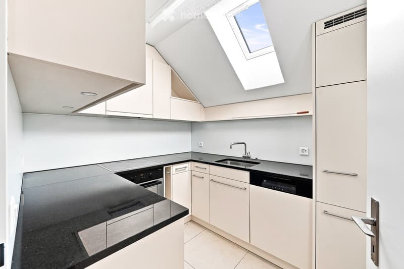 Modern kitchen with white cabinets, black countertops, stainless steel appliances, and a skylight window.