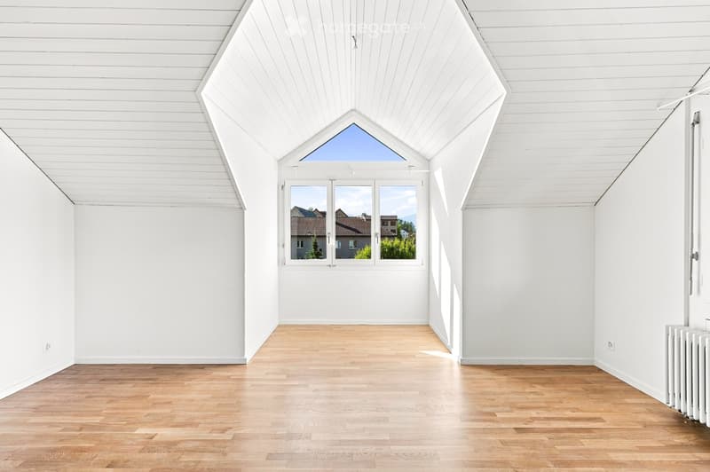 Completely empty room with white walls, wooden floor, and large windows offering a view of the outside. No furniture or equipment present.