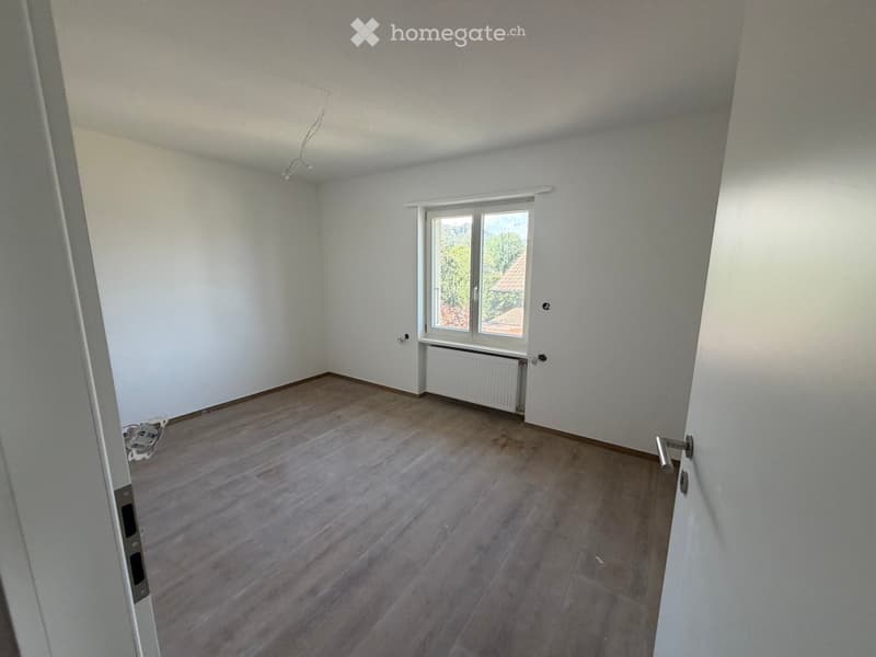 Empty room with wooden flooring, white walls, and a window with a radiator below it. No furniture or personal items are present.