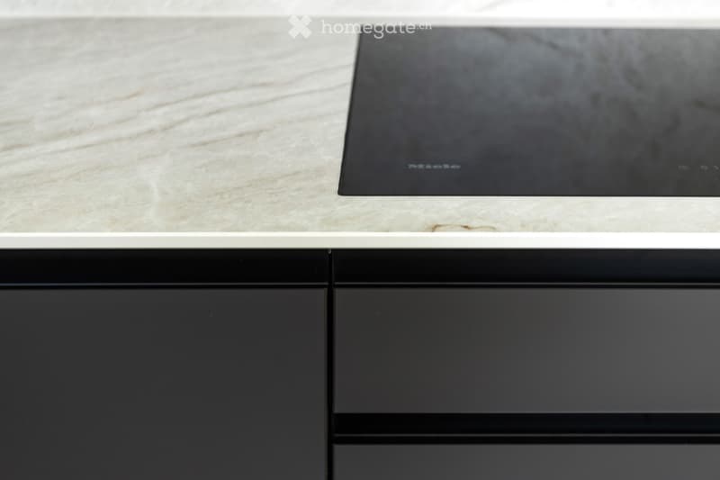 Modern kitchen with a sleek black induction cooktop on a light marble countertop, surrounded by dark cabinets.