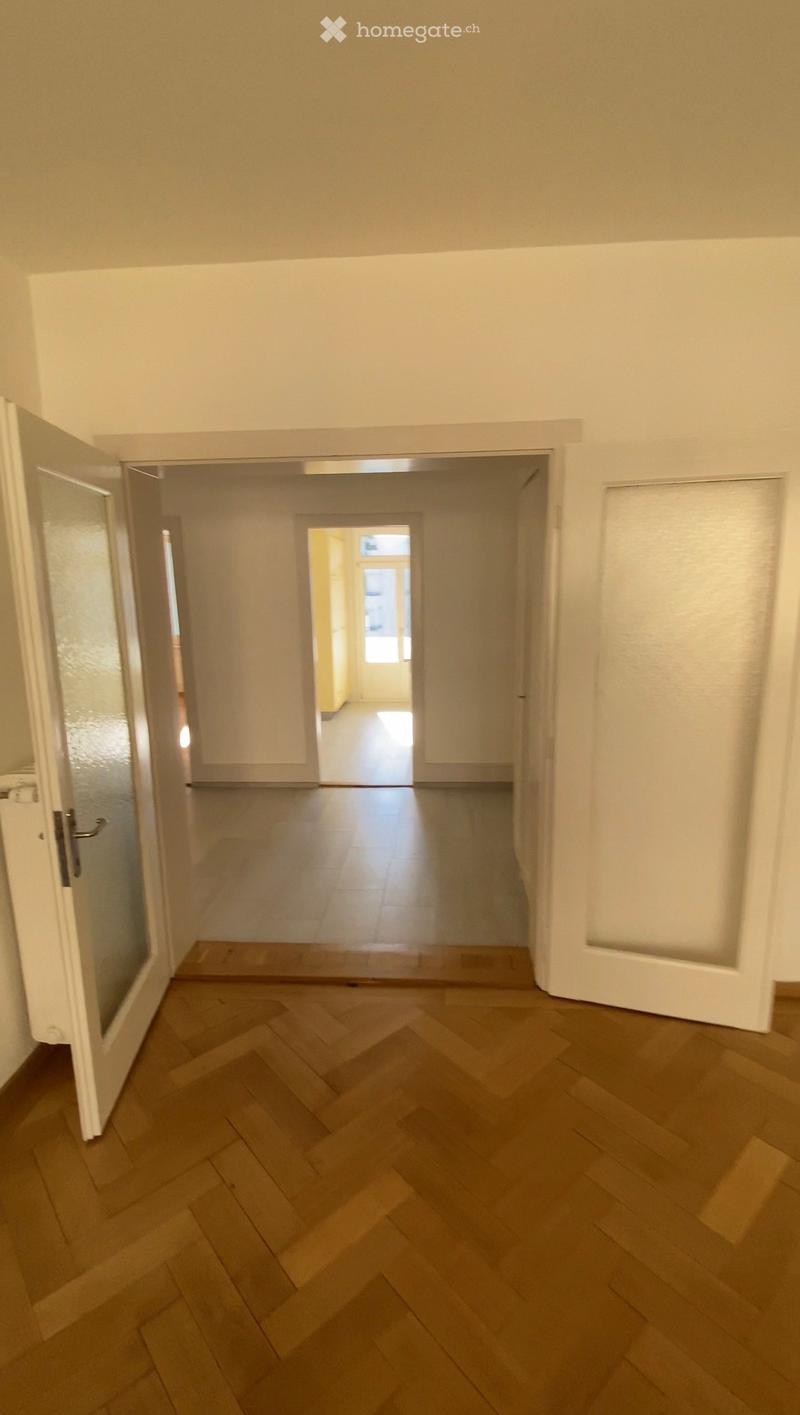 Empty hallway with wooden herringbone flooring, white walls, and multiple doors leading to other rooms.