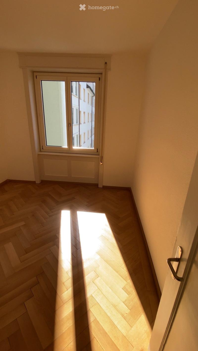 Empty hallway with wooden herringbone flooring and a large window at the end, allowing natural light to enter.