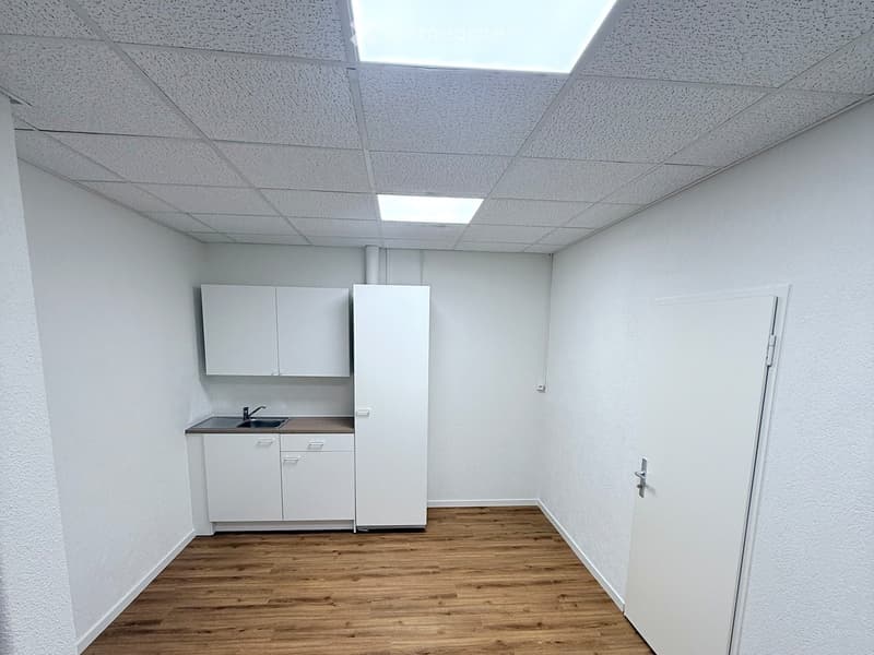 Minimalist kitchen area with white cabinets, a sink, and a refrigerator, featuring wooden flooring and white walls.