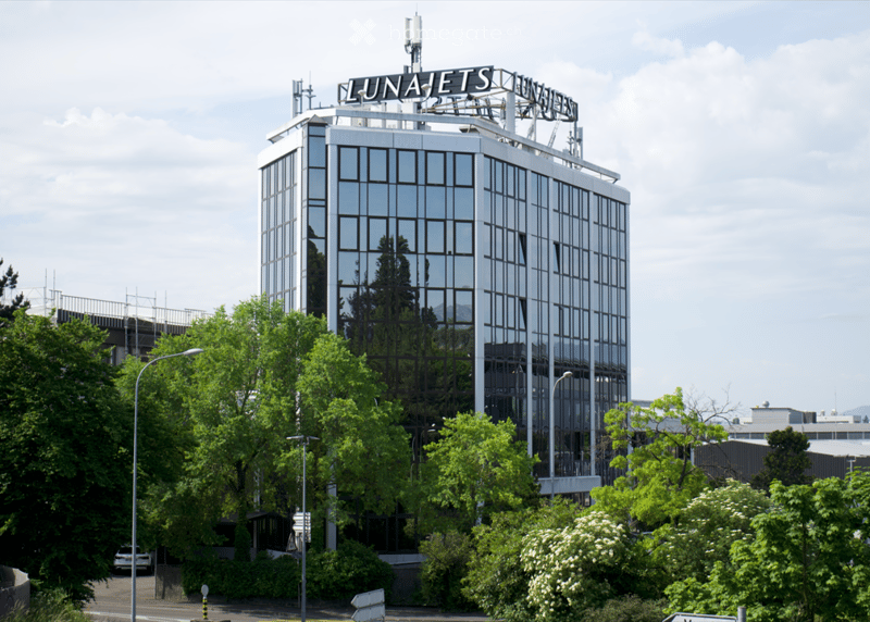 Modern multi-story building with reflective glass windows and a prominent sign reading "LUNAJETS" on the roof.