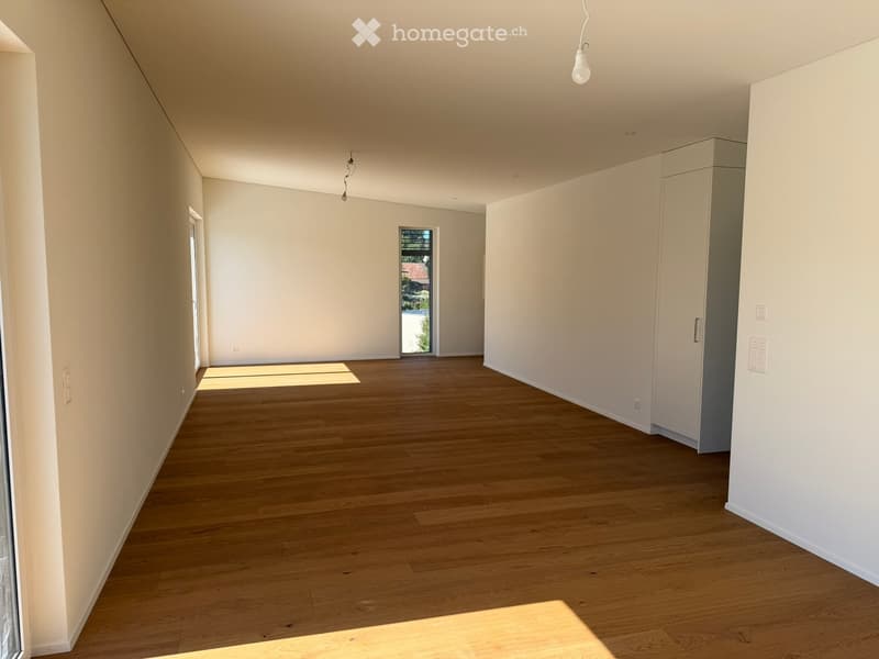 Empty room with wooden flooring, white walls, and built-in cabinets. Natural light streams in from a large window and a door leading outside.