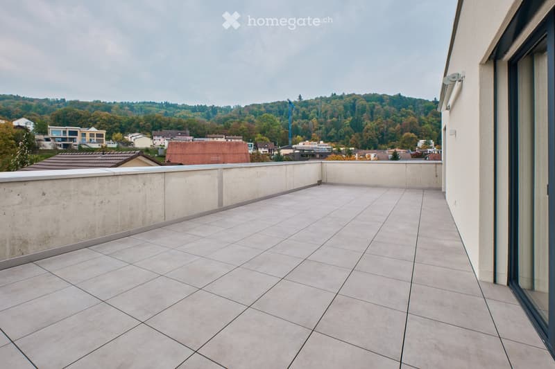 Balcony with tiled floor, low concrete railing, and scenic view of a town and forested hills in the background.