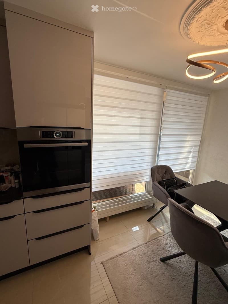Modern kitchen with built-in oven, sleek cabinets, dining table with chairs, and a decorative rug.