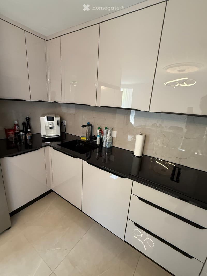 Modern kitchen with white cabinets, black countertops, and stainless steel appliances. Features a coffee maker, sink, and oven.