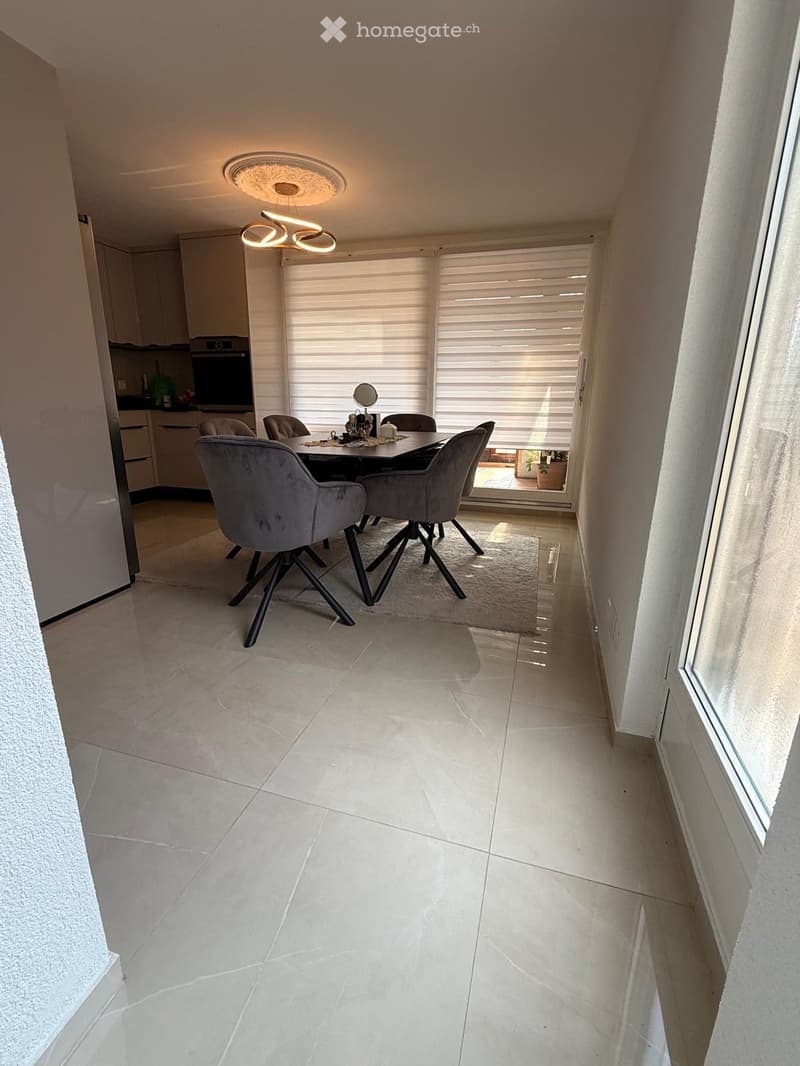 Modern dining area with a sleek black dining table, grey upholstered chairs, and a built-in oven in the adjacent kitchen area.