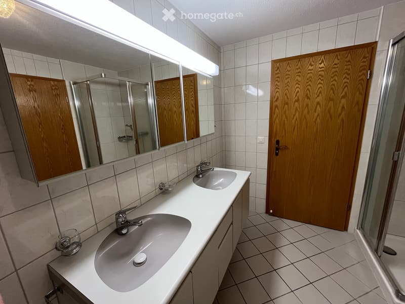 Modern bathroom with two sinks, a large mirror, wooden cabinets, and tiled walls and floor.