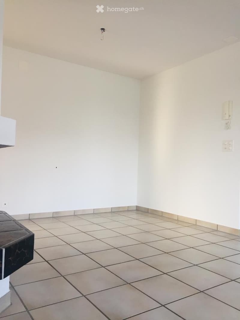Empty room with tiled floor and white walls, featuring a single electrical outlet and a small black object on the floor.