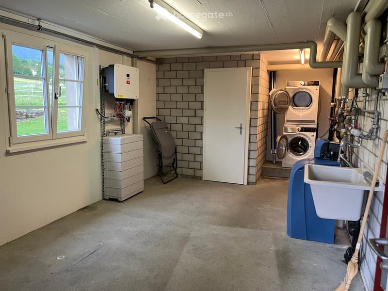 Utility room with washing machine, dryer, water tank, sink, and a door leading to another area.