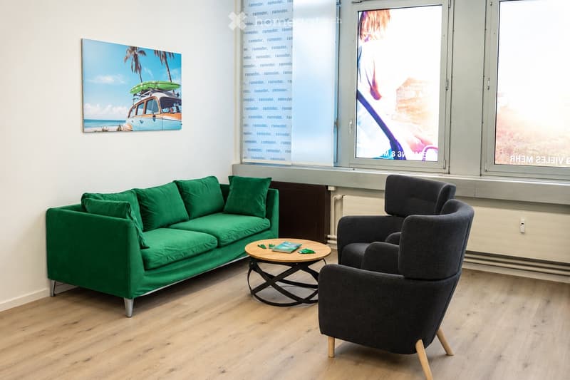 Modern living room with green sofa, dark grey armchair, round coffee table, and a large picture frame on the wall.