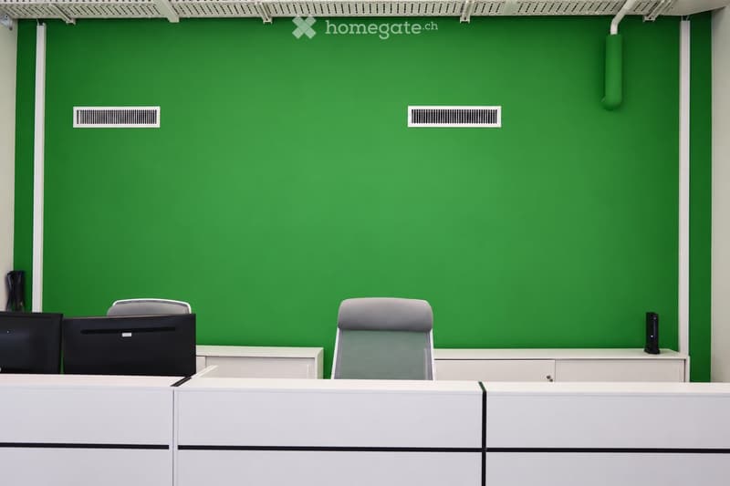 Office space with green accent wall, white desks, grey chairs, and computer setup.