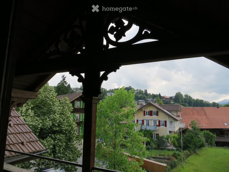 View from a balcony overlooking a residential area with houses, trees, and distant mountains.