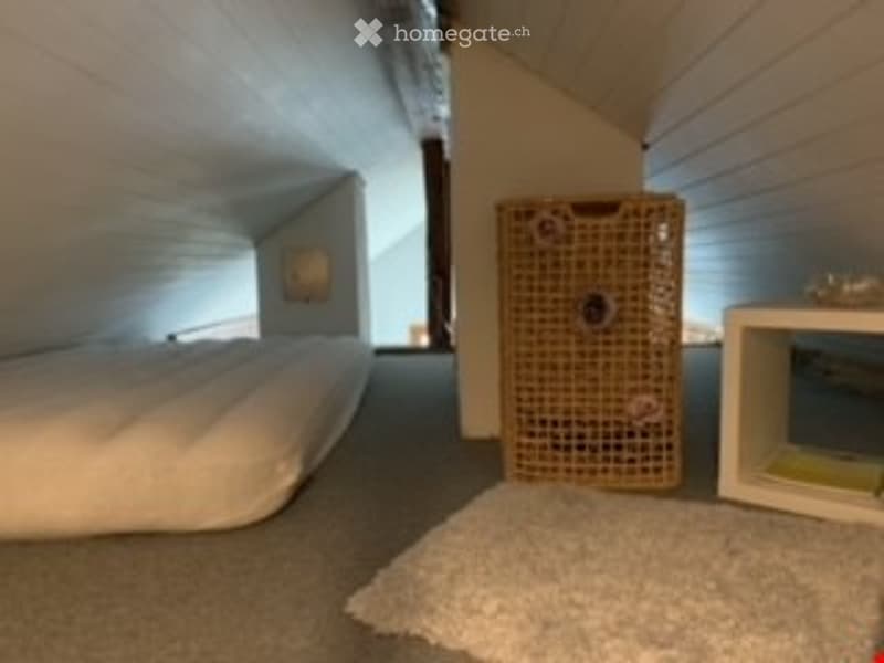 Cozy attic bedroom with slanted ceilings, white bed, cat carrier, small shelf, and a rug on the floor.