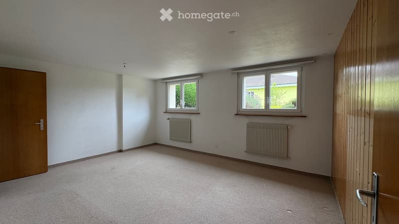 Empty room with white walls, carpeted floor, two windows, and radiators. No furniture or equipment present.
