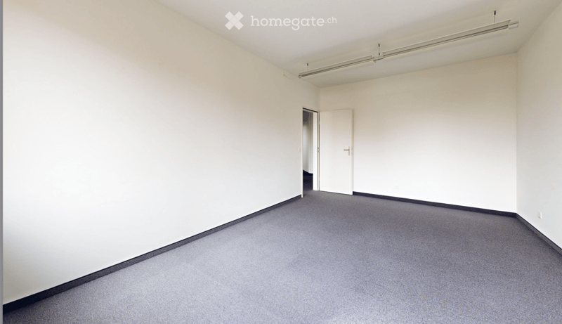 Empty room with white walls, grey carpet, and a single door leading to another space.