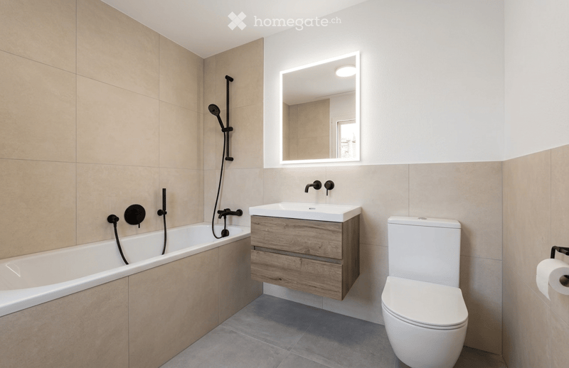 Modern bathroom with a bathtub, sink, toilet, and illuminated mirror. Beige tiles and wooden vanity.