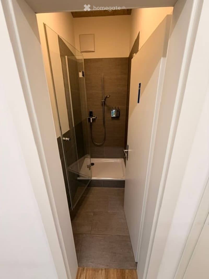 Modern bathroom with a glass-enclosed shower stall, tiled floor, and white walls.