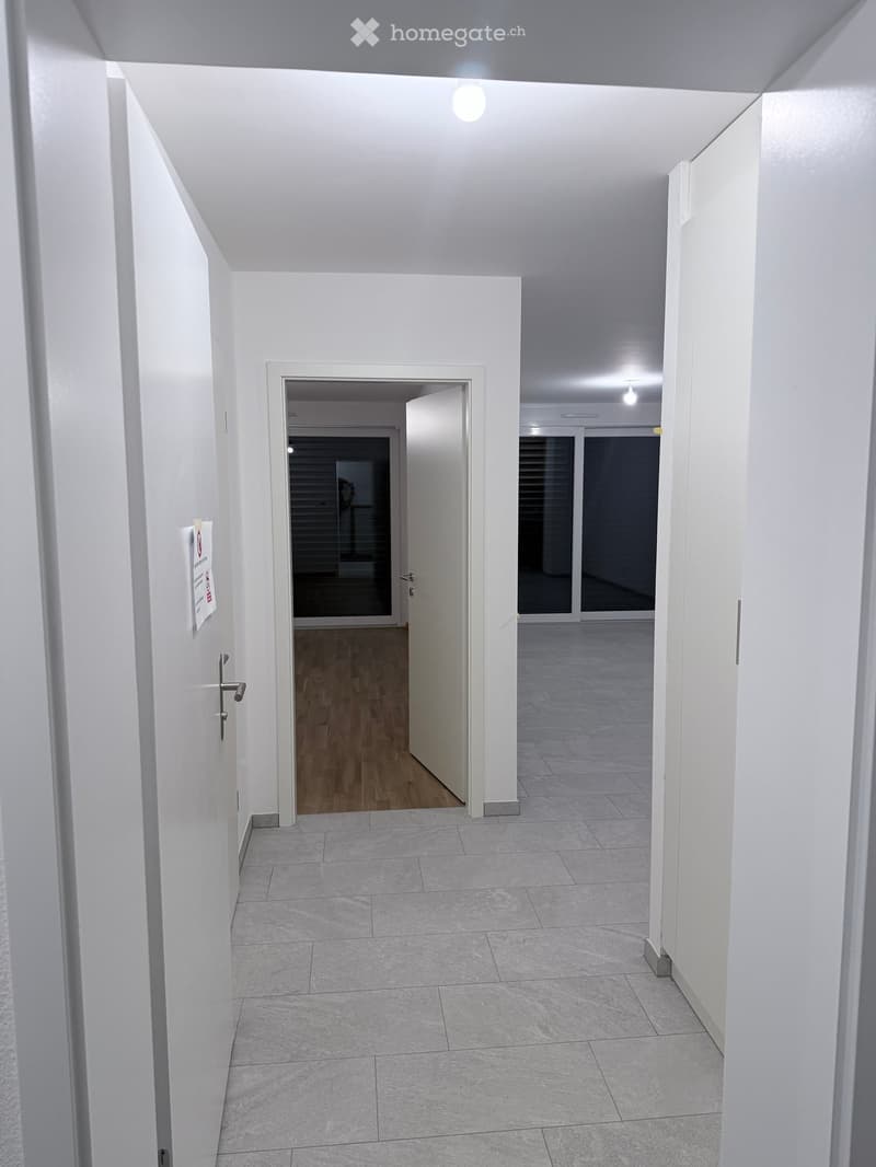Empty hallway with white walls, tiled floor, and two open doors leading to adjacent rooms.