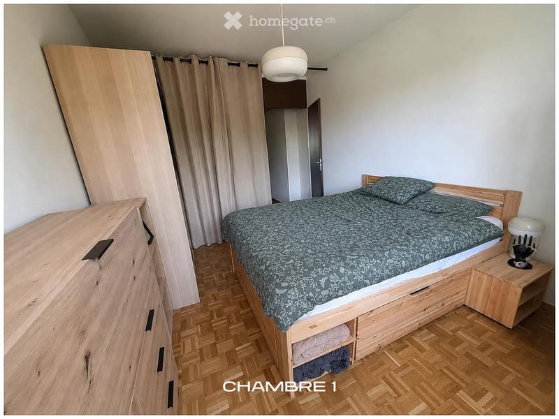 Bedroom with wooden bed, nightstand, wardrobe, and curtains. Wooden floor and white walls.