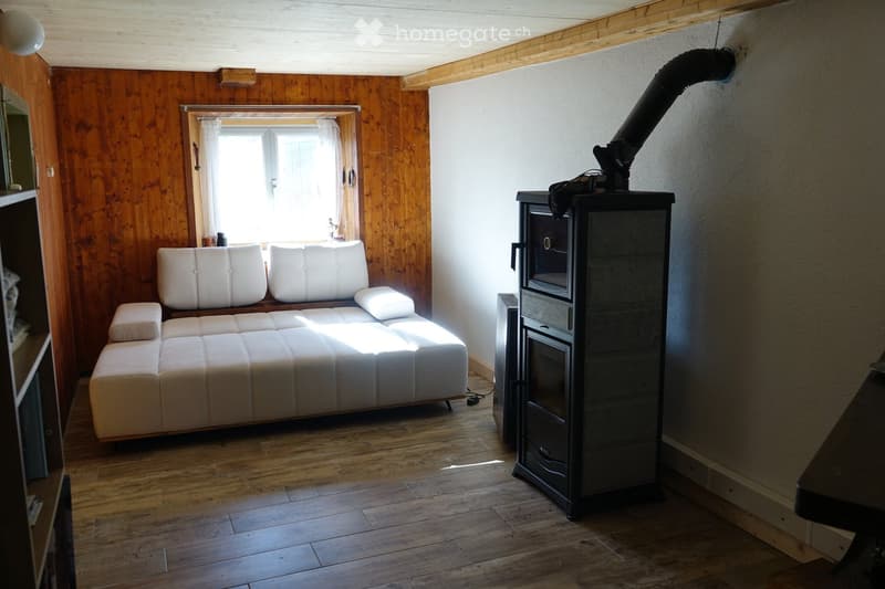 Cozy living room with white leather sofa, ottoman, wood stove, and wooden walls.