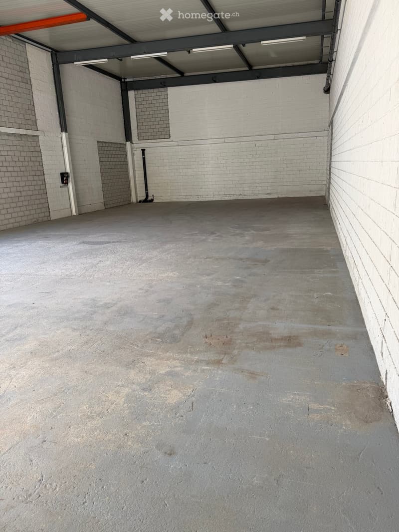 Empty concrete garage space with white brick walls, metal ceiling beams, and fluorescent lighting.