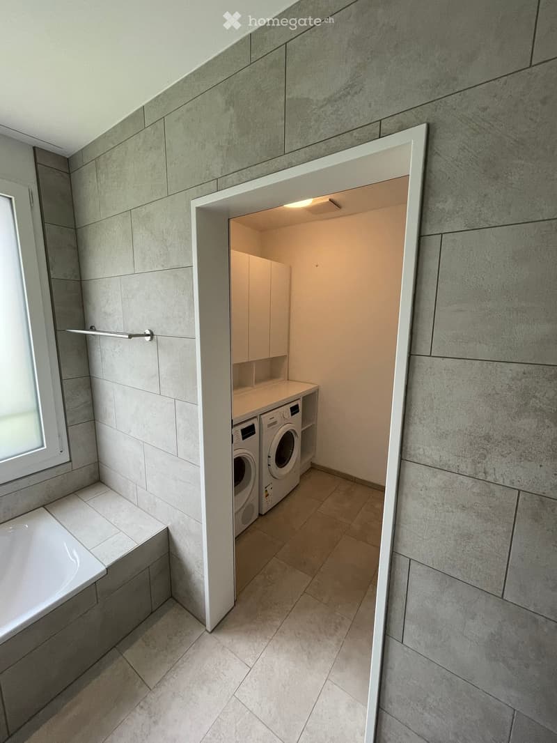 Modern bathroom with a bathtub, a washing machine, and built-in cabinets.