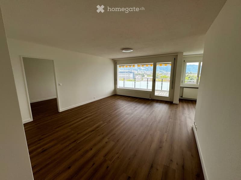 Empty room with wooden flooring, large windows, and a sliding glass door leading to a balcony.