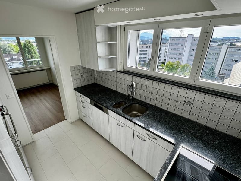 Modern kitchen with white cabinets, granite countertop, double sink, and large windows offering a city view.