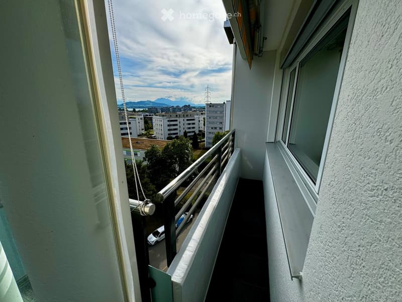 Balcony with metal railing, overlooking a cityscape with buildings, trees, and parked cars.