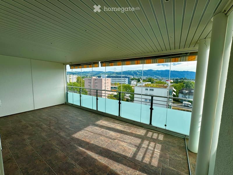 Balcony with tiled floor, glass railing, and a view of the city and mountains.