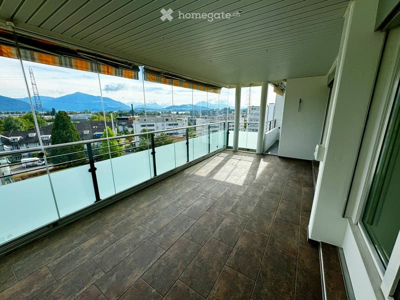 Spacious balcony with tiled flooring, glass railings, and scenic mountain views.
