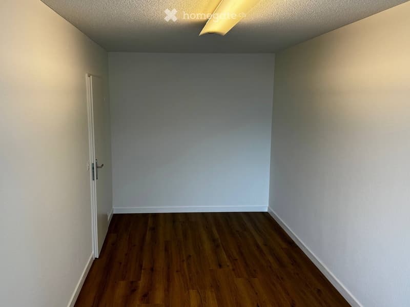 Empty room with wooden flooring, white walls, and a single door on the left side.