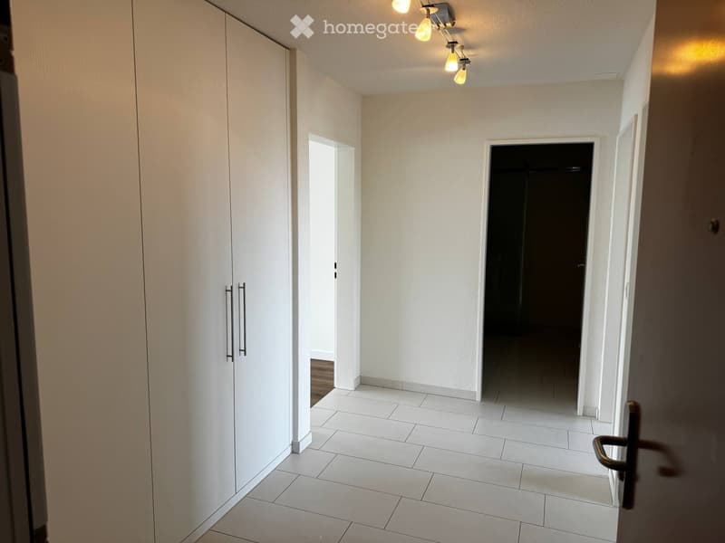 Empty hallway with white tiled flooring, white walls, and a built-in white closet on the left side. The hallway has two open doorways leading to other rooms.