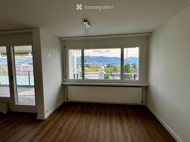 Empty room with wooden flooring, white walls, large windows offering a scenic view, and a radiator below one window.