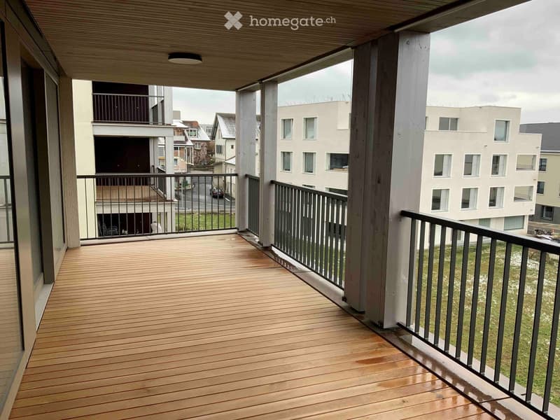 Balcony with wooden decking, metal railing, and view of surrounding buildings and greenery.