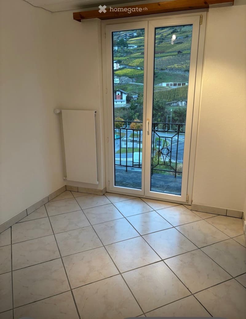 Empty room with tiled floor, white walls, and a sliding glass door leading to a balcony with a view of the countryside.