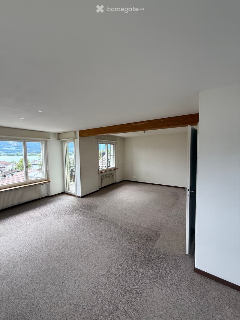 Empty room with carpeted floor, white walls, large windows, and a door leading to another space.