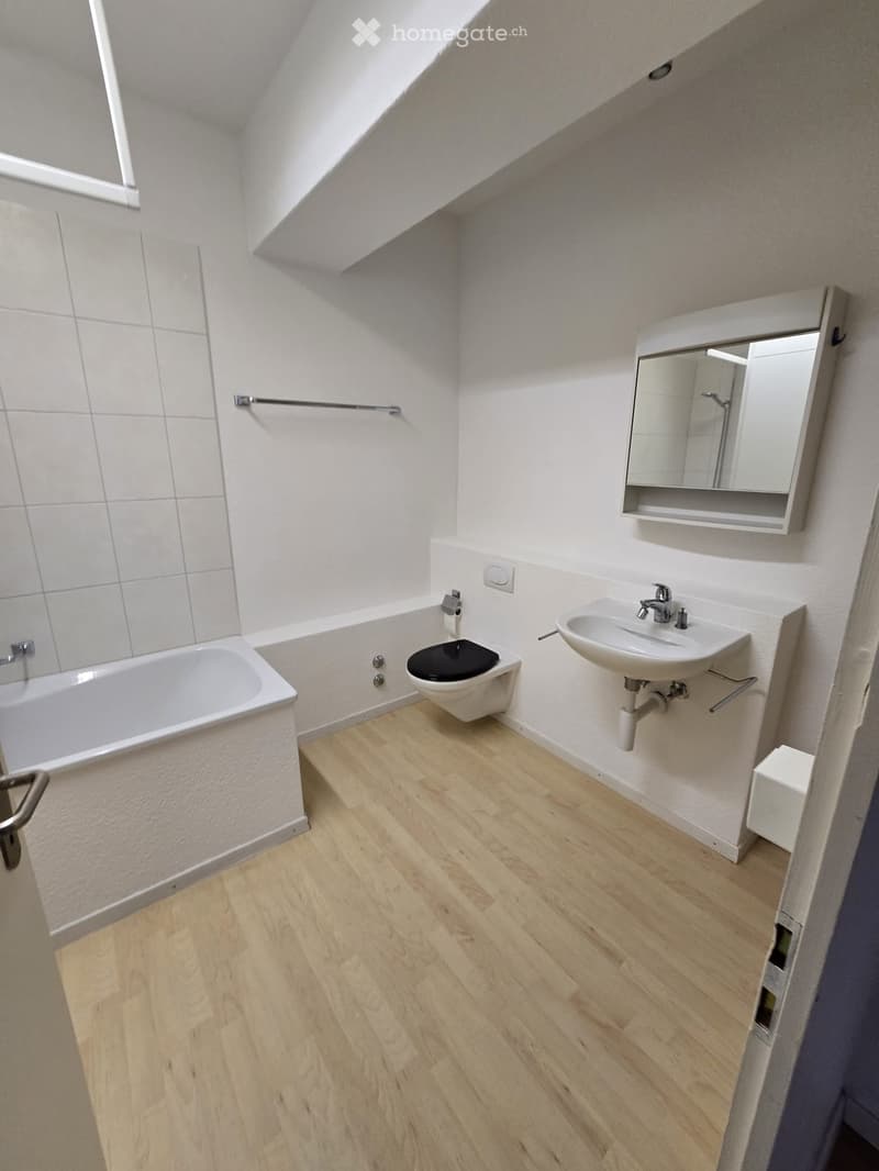 Modern bathroom with wooden flooring, white tiled walls, bathtub, toilet, sink, and a mirror cabinet.