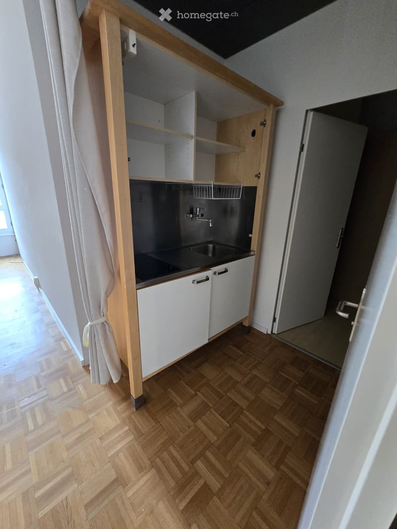 Empty kitchen area with wooden herringbone flooring, white cabinets, and a sink. No appliances or furniture are present.