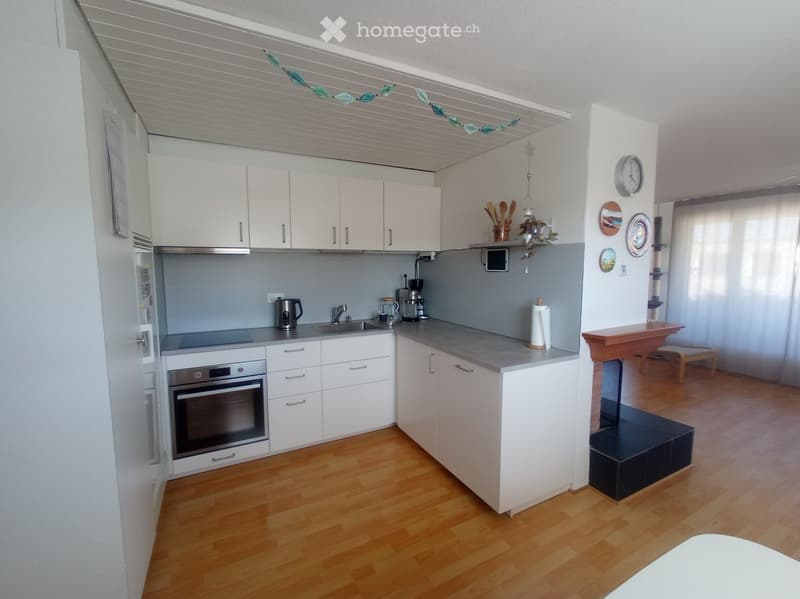 Modern kitchen with white cabinets, stainless steel appliances, wooden flooring, and a small dining area visible in the background.