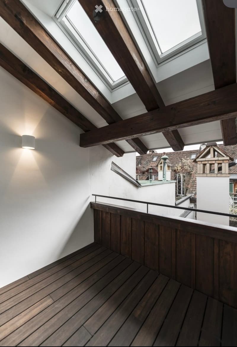 Wooden hallway with exposed beams, skylights, and a view of the cityscape through a glass railing.