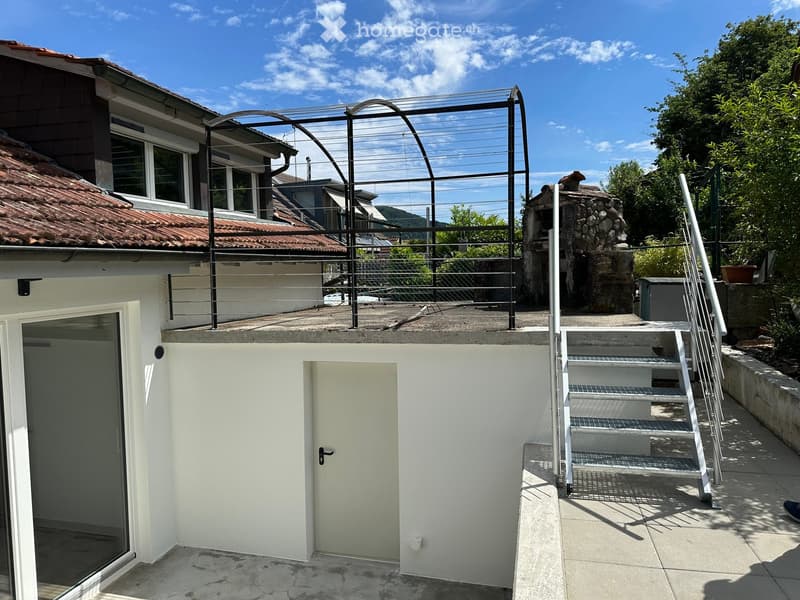 Outdoor area with a staircase leading up to a rooftop terrace, featuring a metal railing and a stone chimney structure.