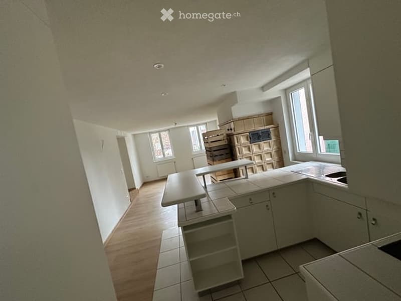 Bright, modern kitchen with white cabinets, a central island, and a dining table. The space features wooden flooring and large windows allowing natural light to fill the room.